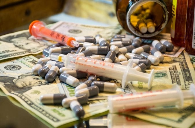 Big Pharma pills and syringes laying on money