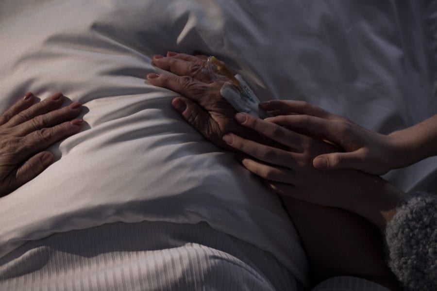 Woman holding hands of dying mom