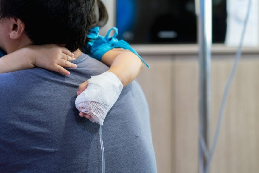 Child with cancer on IV being held in father's arms. we can only see her hand and his back