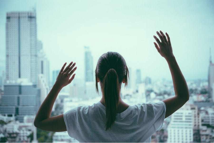 Woman standing at the window of a big city feeling lack of human connection