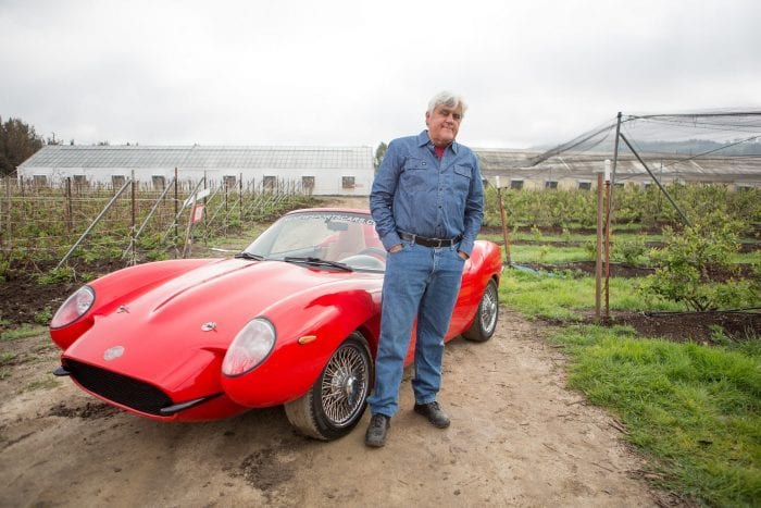 Jay Leno standing in front of his red hemp sports car