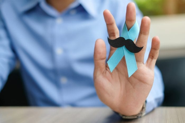 man hand holding up blue ribbon with moustache sticker