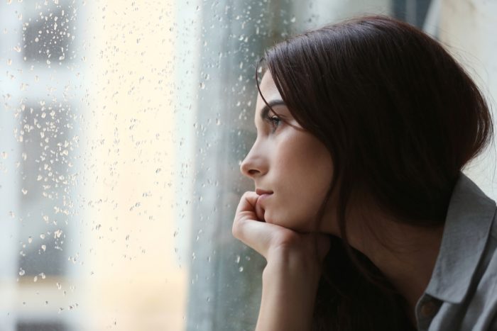 depressed girl looking out rainy window