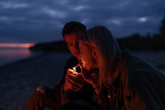 sex and cannabis represented by young couple lighting joint on a beach at night