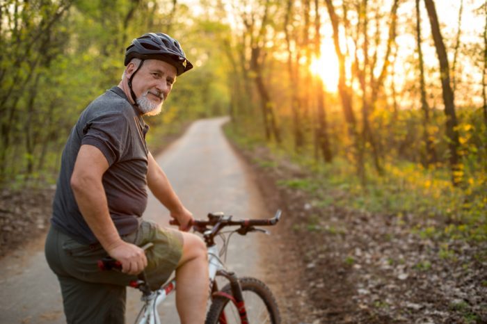 older man no longer living with chronic pain as he rides his bike down a pretty path