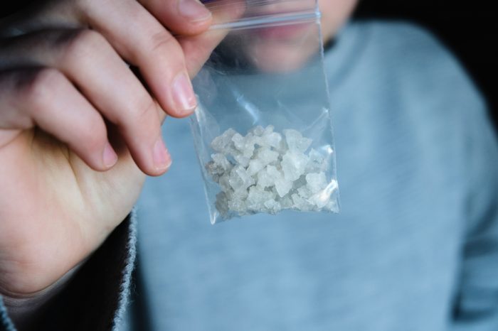 brain damage from meth represented by girl holding baggie with meth crystals