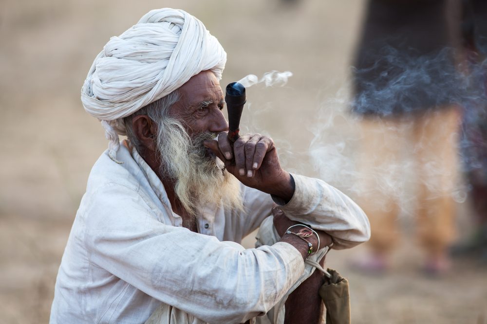 An old man bearded man smokes from a hash pipe. Cannabis hash originates from Central Asia