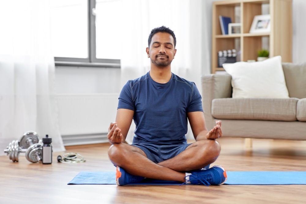 how to heal the mind body and spirit represented by hispanic man meditating next to yoga mat and weights