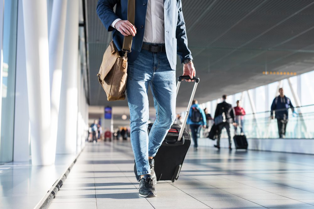 man walking through airport with suitcase on wheels