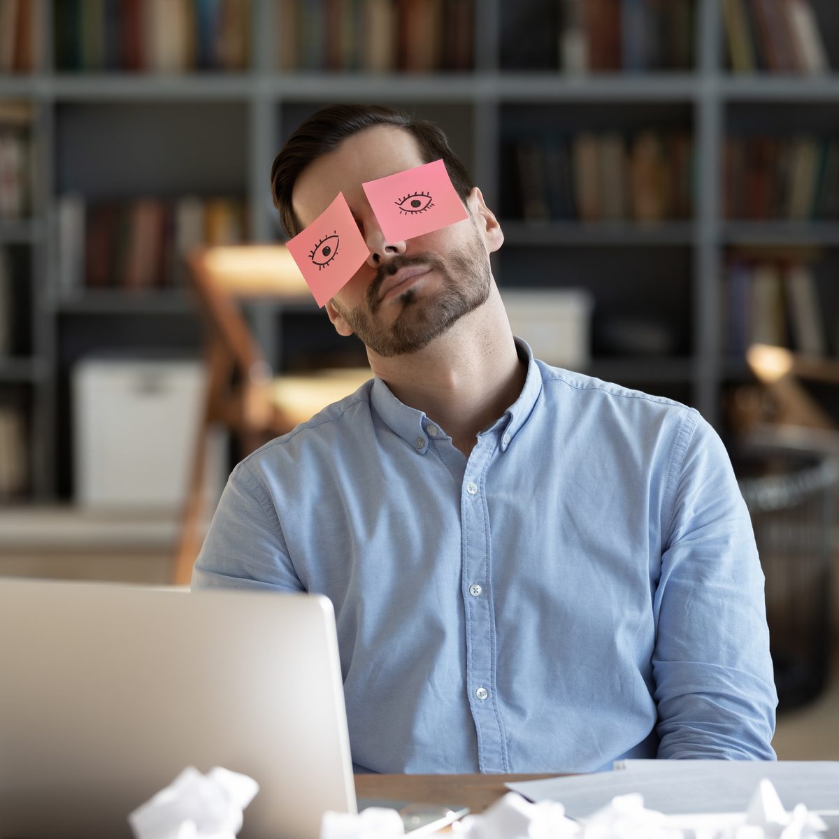burn-out recovery represented by man asleep at his desk with sticky note eyeballs on his face
